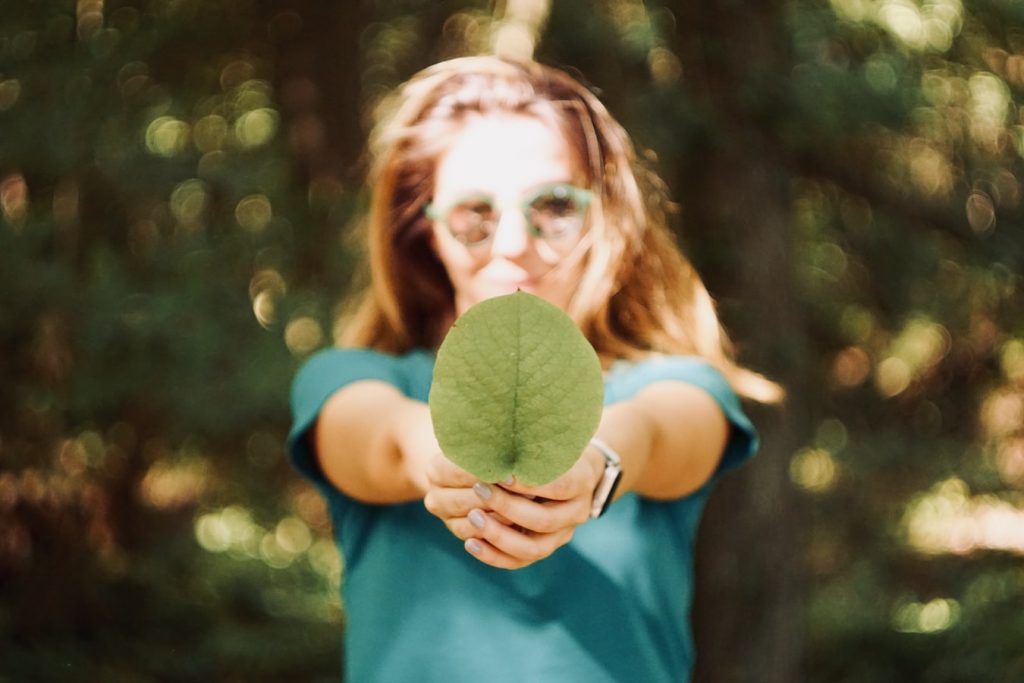 chica sosteniendo una hoja verde en sus manos en símbolo de ecología